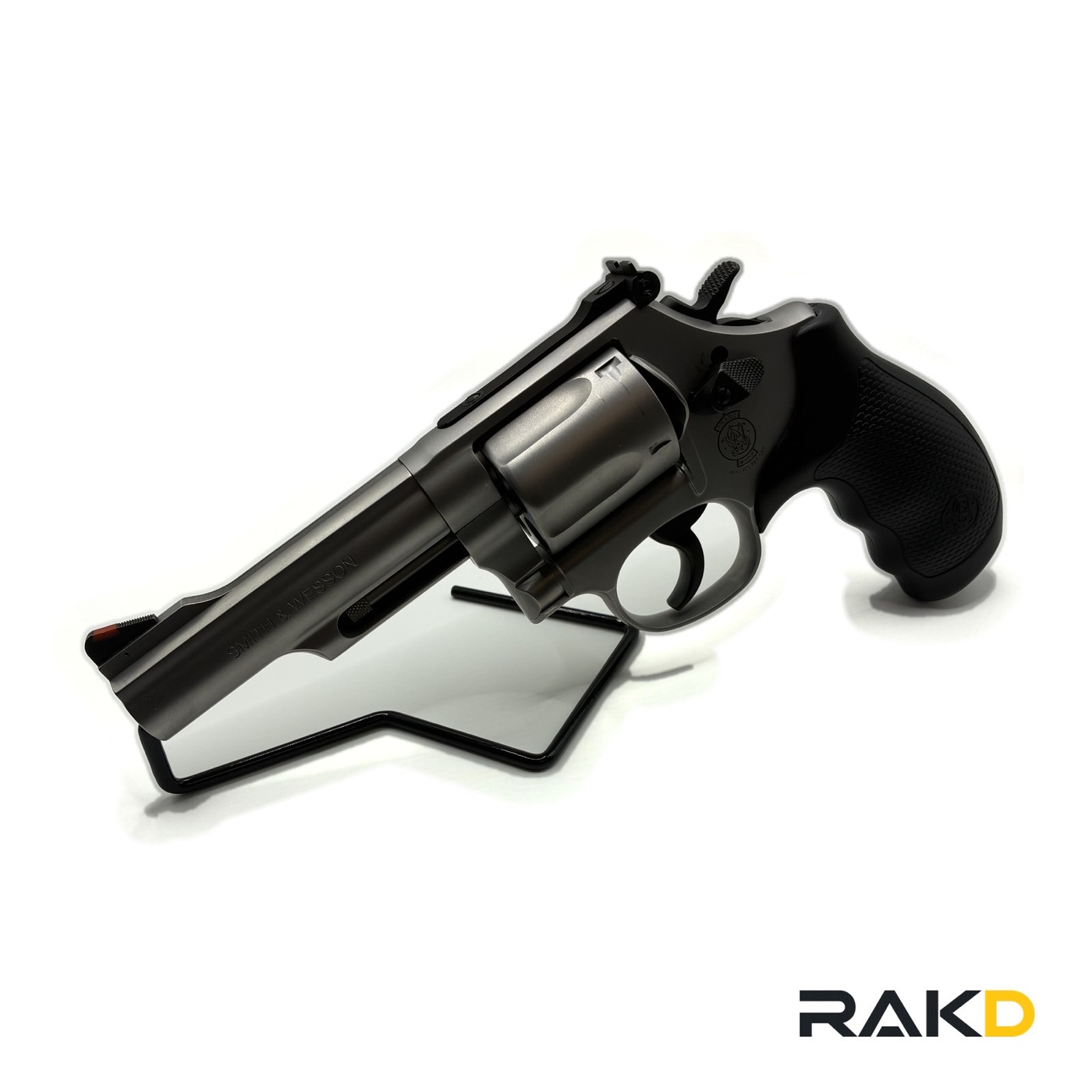 A stainless Smith & Wesson revolver with a four inch barrel photographed from the front quarter, with black rubber grips and a red ramp front sight.